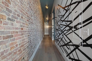 A corridor with a brick wall on one side and a white wall with black geometric patterns on the other. - Lofted Luxury | 5 BR • Sleeps 10 • Downtown! (Frankfort)