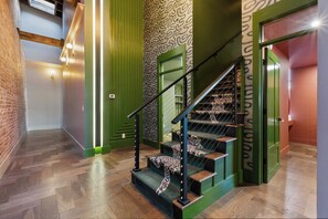 A staircase with a green handrail and leopard print steps, leading to a room with a patterned wall and a brick wall on one side. - Stunning Penthouse | Luxe • Sleeps 19 • Downtown! (Frankfort)