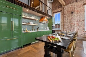 Une cuisine moderne avec des meubles de couleur verte, un plan de travail noir et un coin repas doté d’une longue table dressée pour six personnes.