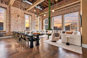 Une pièce spacieuse avec un mur en briques, une grande table à manger entourée de chaises, un canapé et une cheminée.