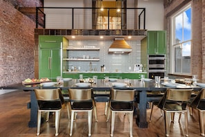 Een moderne keuken met groene kastjes, een centraal eiland en een eethoek met zwarte stoelen.