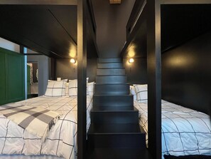 Une chambre avec un escalier central, deux lits avec du linge de lit à rayures et une porte verte.