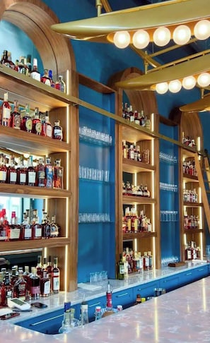 A bar area with shelves of liquor bottles, a bar counter, and a ceiling with lights. - Suite Luxury | Designer • Ideal Downtown Location! (Frankfort)