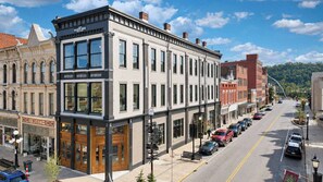 A street view with a building featuring a modern facade, a visible storefront with a sign, and parked cars along the road. - Suite Luxury | Designer • Ideal Downtown Location! (Frankfort)