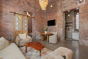Een ruime woonkamer met een bakstenen muur, een flatscreen televisie aan de wand, een houten salontafel en een bank met een zachte plaid.