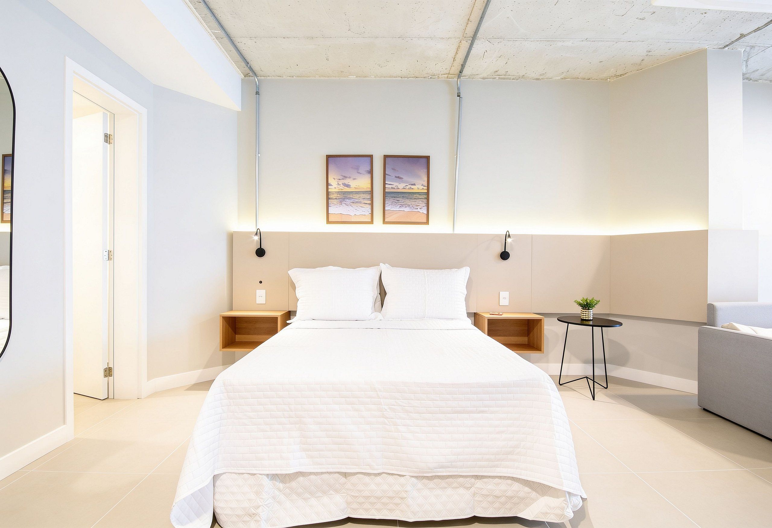 A modern bedroom with a large bed, bedside tables, a small round table, and two framed pictures on the wall.