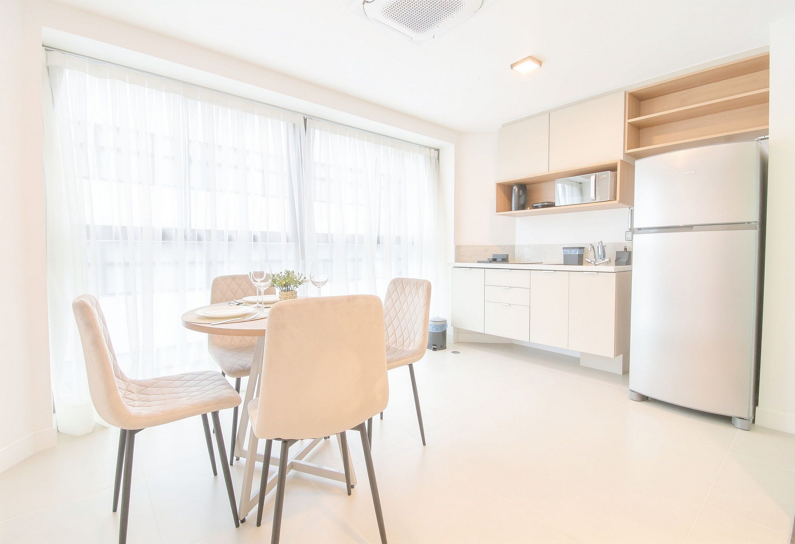 Una cocina moderna con refrigerador empotrado, muebles blancos y un comedor con mesa redonda y sillas acolchadas.
