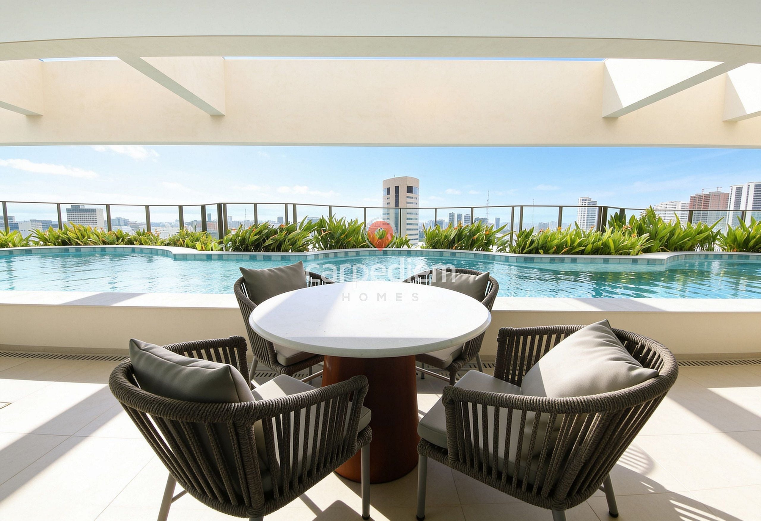 A rooftop pool area with a round table and wicker chairs, surrounded by a railing and a view of the city skyline.