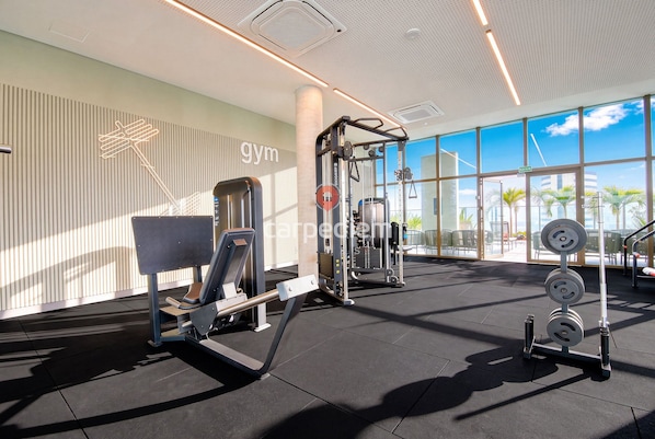 A gym with exercise equipment, large windows, and a view of palm trees.