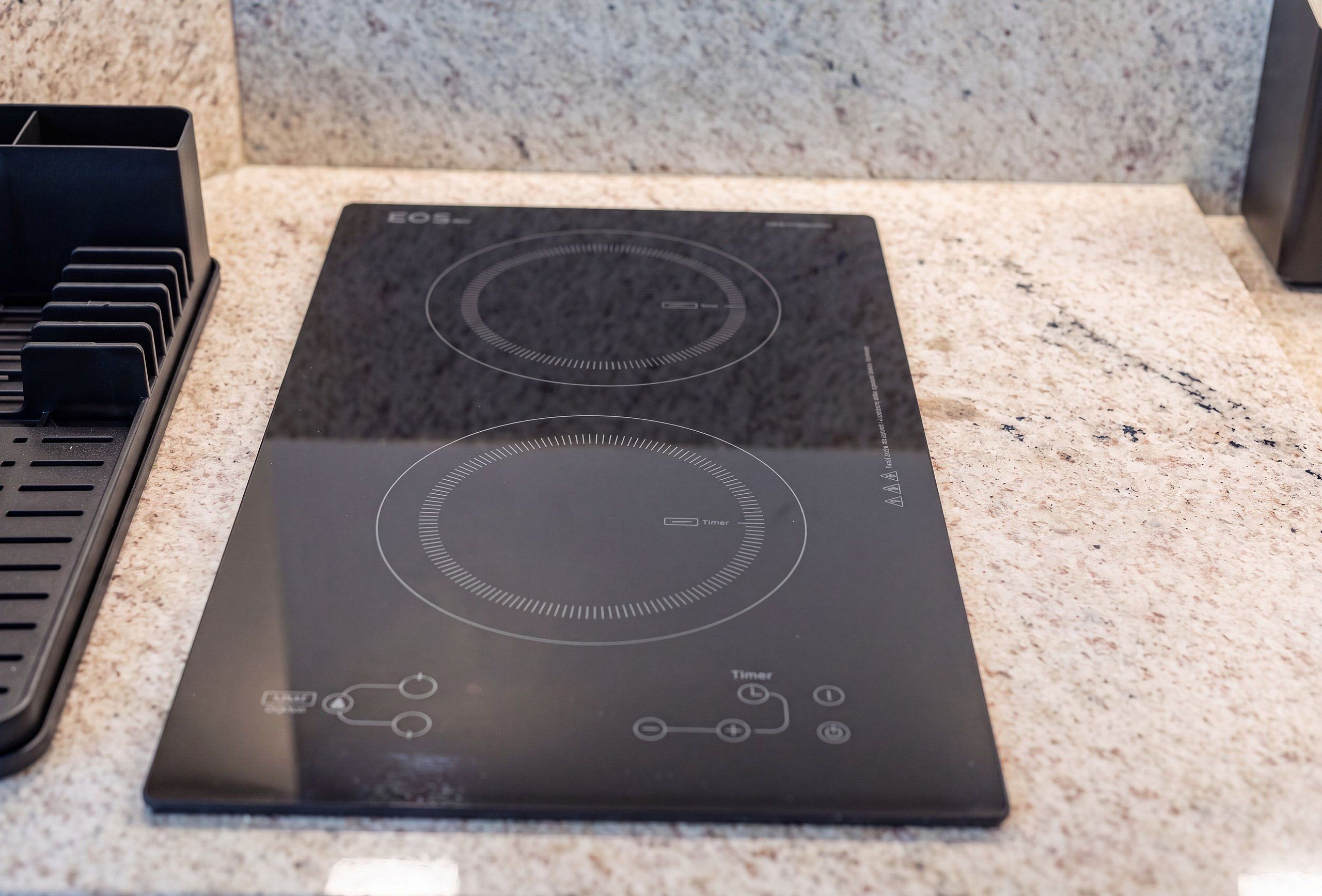 Een zwarte inductiekookplaat met timer en bedieningspaneel, geplaatst op een granieten aanrecht.