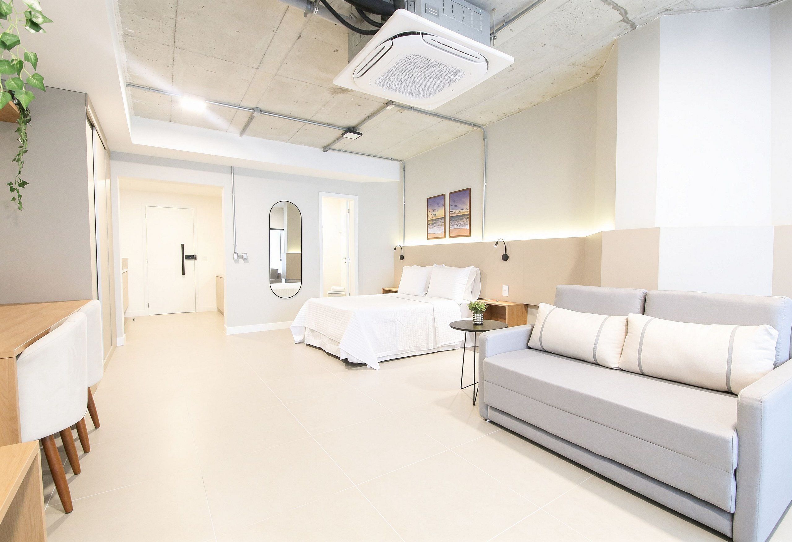 A modern hotel room with a bed, a sofa, a small table, and a mirror.