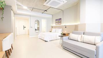A modern hotel room with a bed, a sofa, a small table, and a mirror.