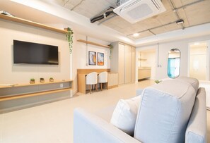 A modern living room with a flat-screen TV, a sofa, and a dining area with chairs.