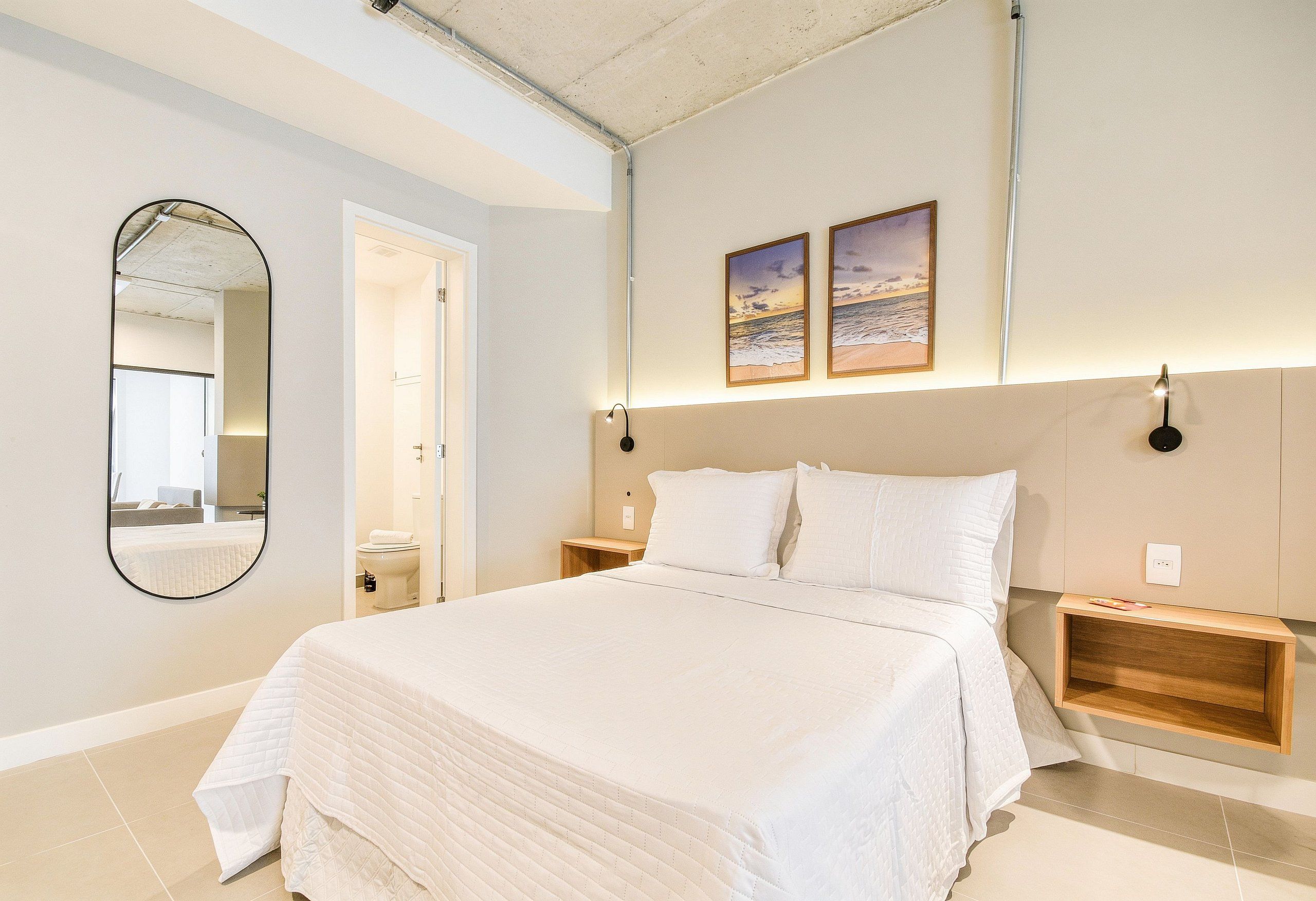 A bedroom with a large bed, a mirror, two bedside tables, and a wall-mounted light fixture.