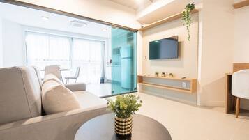 Ein modernes Wohnzimmer mit einer Couch, einem Couchtisch, einem an der Wand befestigten Fernseher und einer Glastür, die auf einen Balkon führt.