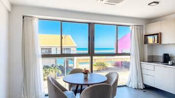 A modern kitchen with a view of the beach, a dining area with chairs and a table, and a large window with curtains.