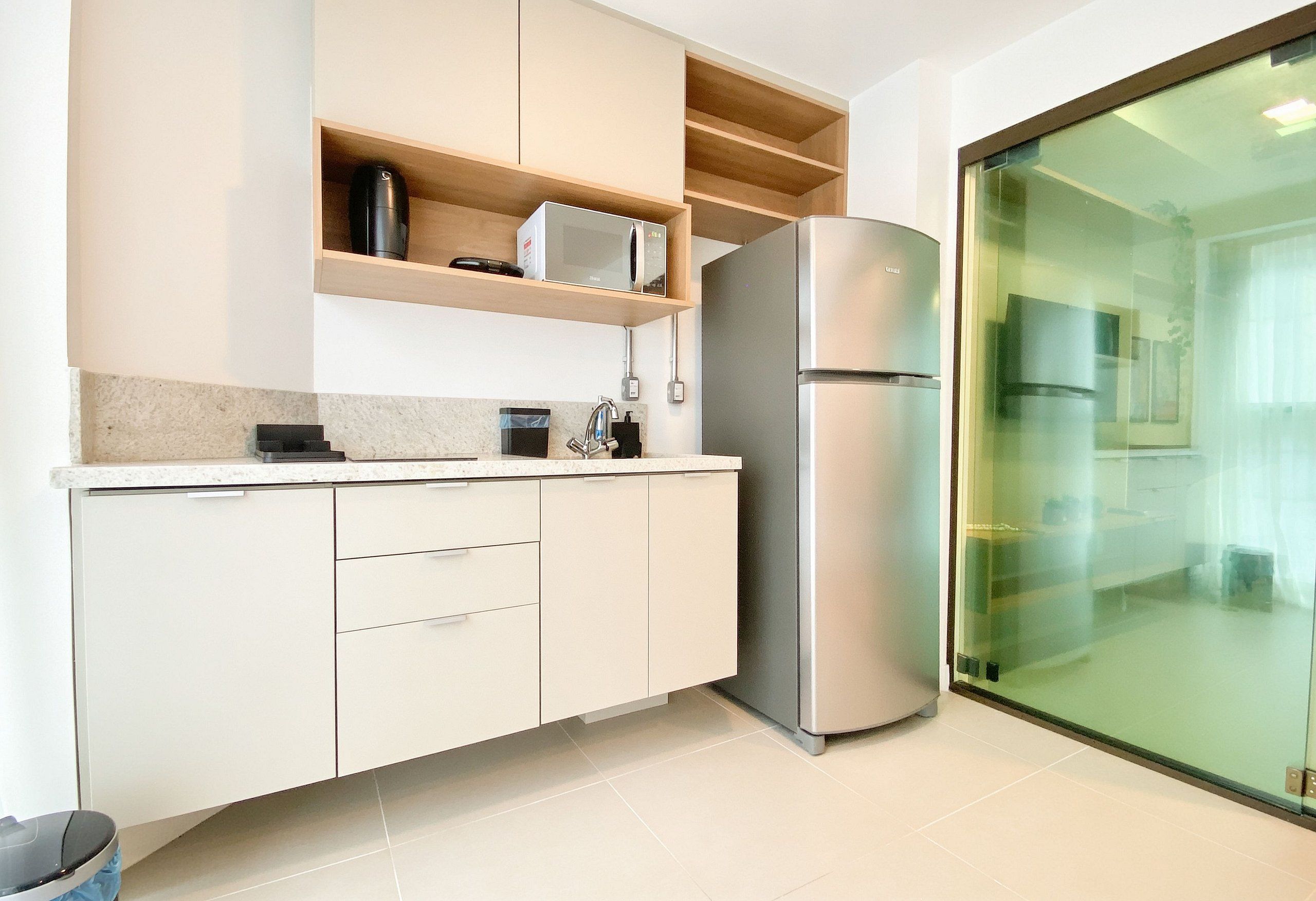 A modern kitchen with a built-in microwave, a stainless steel refrigerator, and a glass door leading to a balcony.