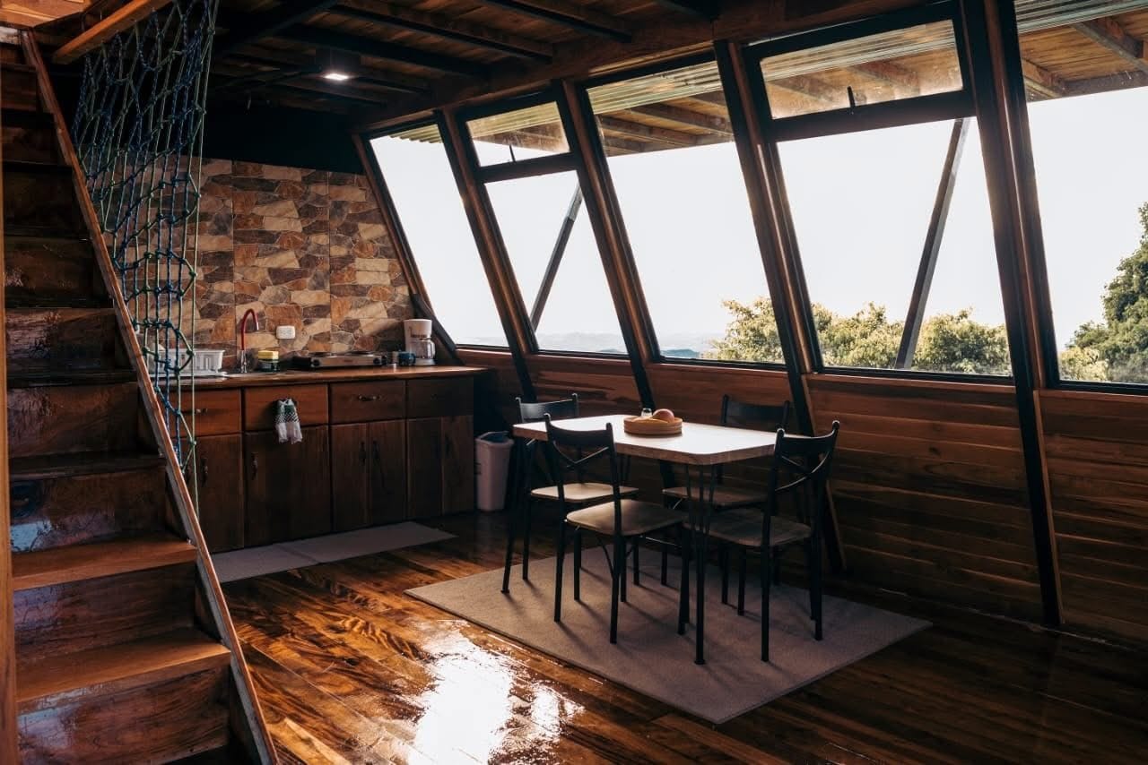 A wooden interior with a kitchen area, a dining table with chairs, and a staircase.
