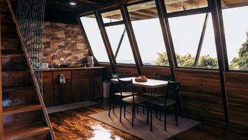 A wooden interior with a kitchen area, a dining table with chairs, and a staircase.