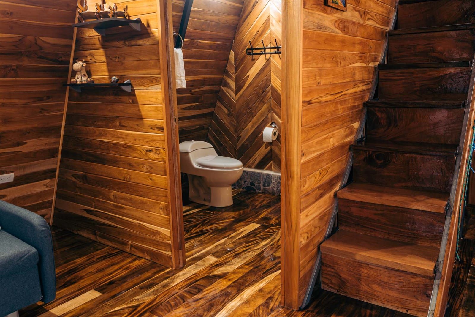 A wooden interior with a wooden staircase, a toilet, and a blue chair.