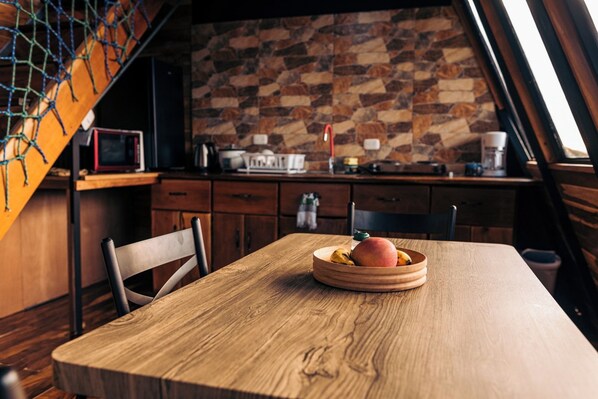 A wooden dining table with a fruit bowl, a chair, and a kitchen in the background with a stone wall. - Torremar House Monteverde (Provincia de Puntarenas)