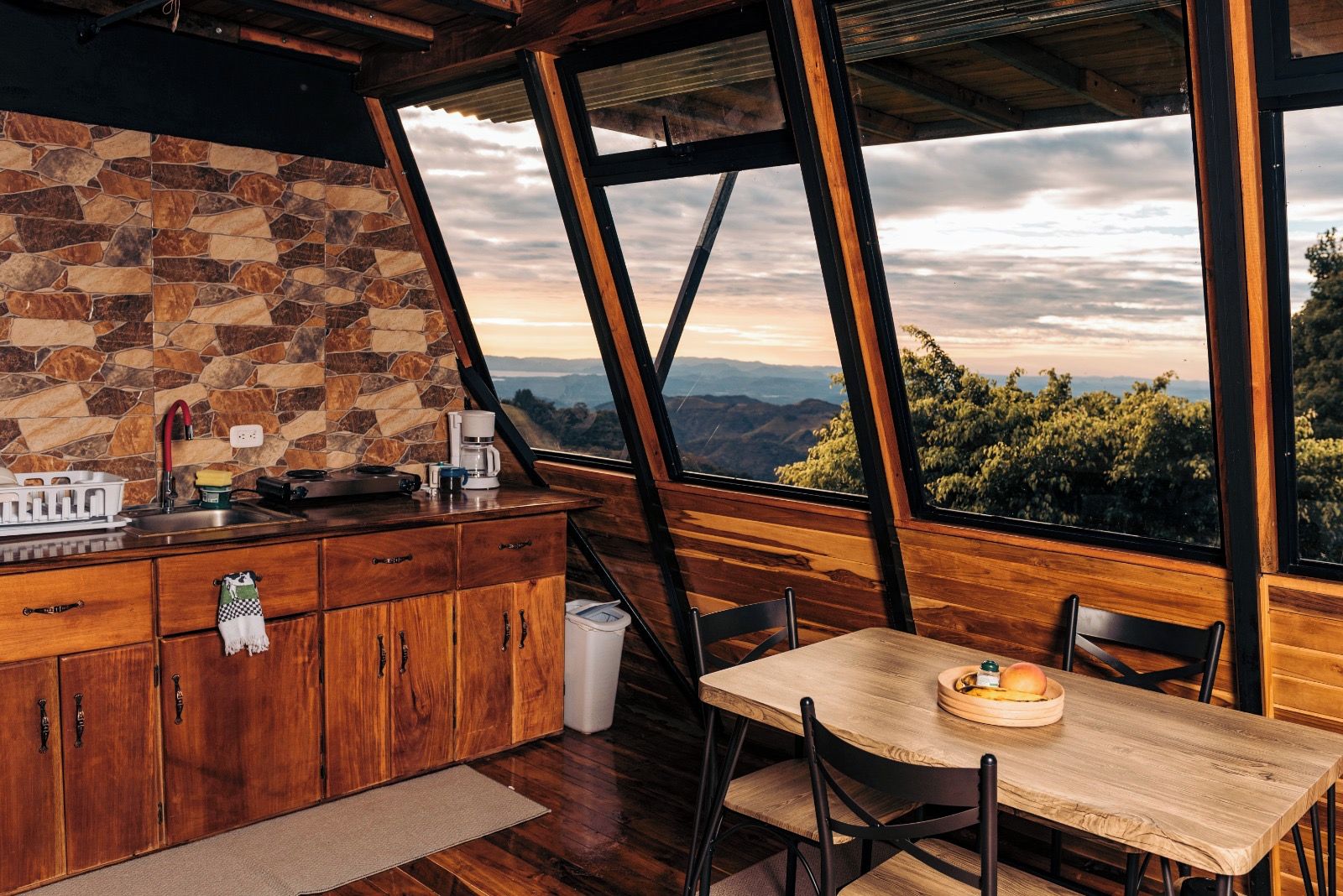 A kitchen with a stone backsplash, wooden cabinets, and a view of the mountains through large windows.