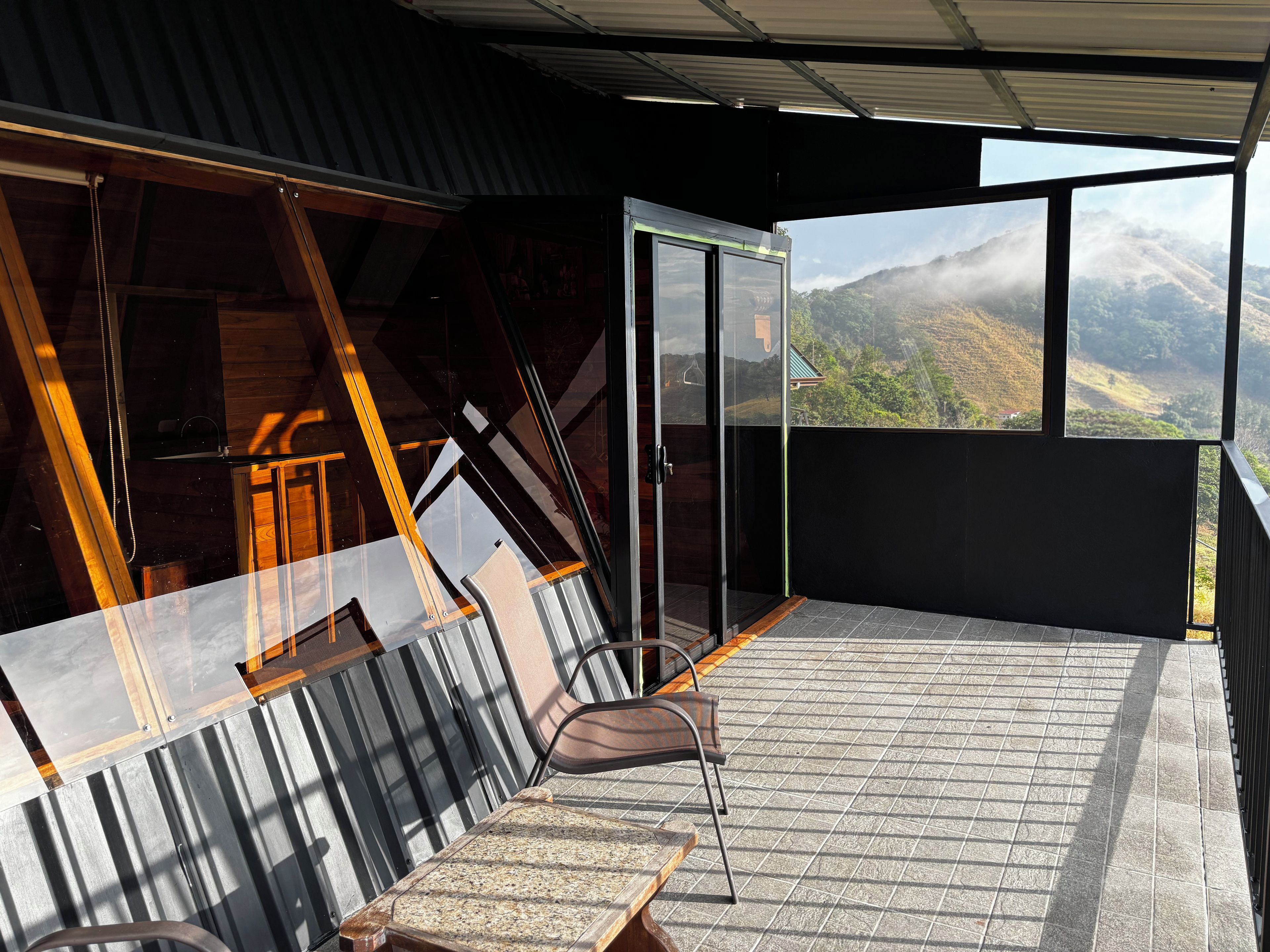 A balcony with a view of a mountainous landscape, a chair, and a table.