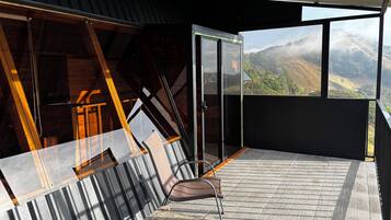 A balcony with a view of a mountainous landscape, a chair, and a table.