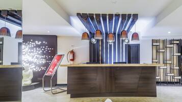 Una zona de recepción moderna con suelo de mármol, un mostrador de recepción, un extintor y un elemento decorativo en la pared.