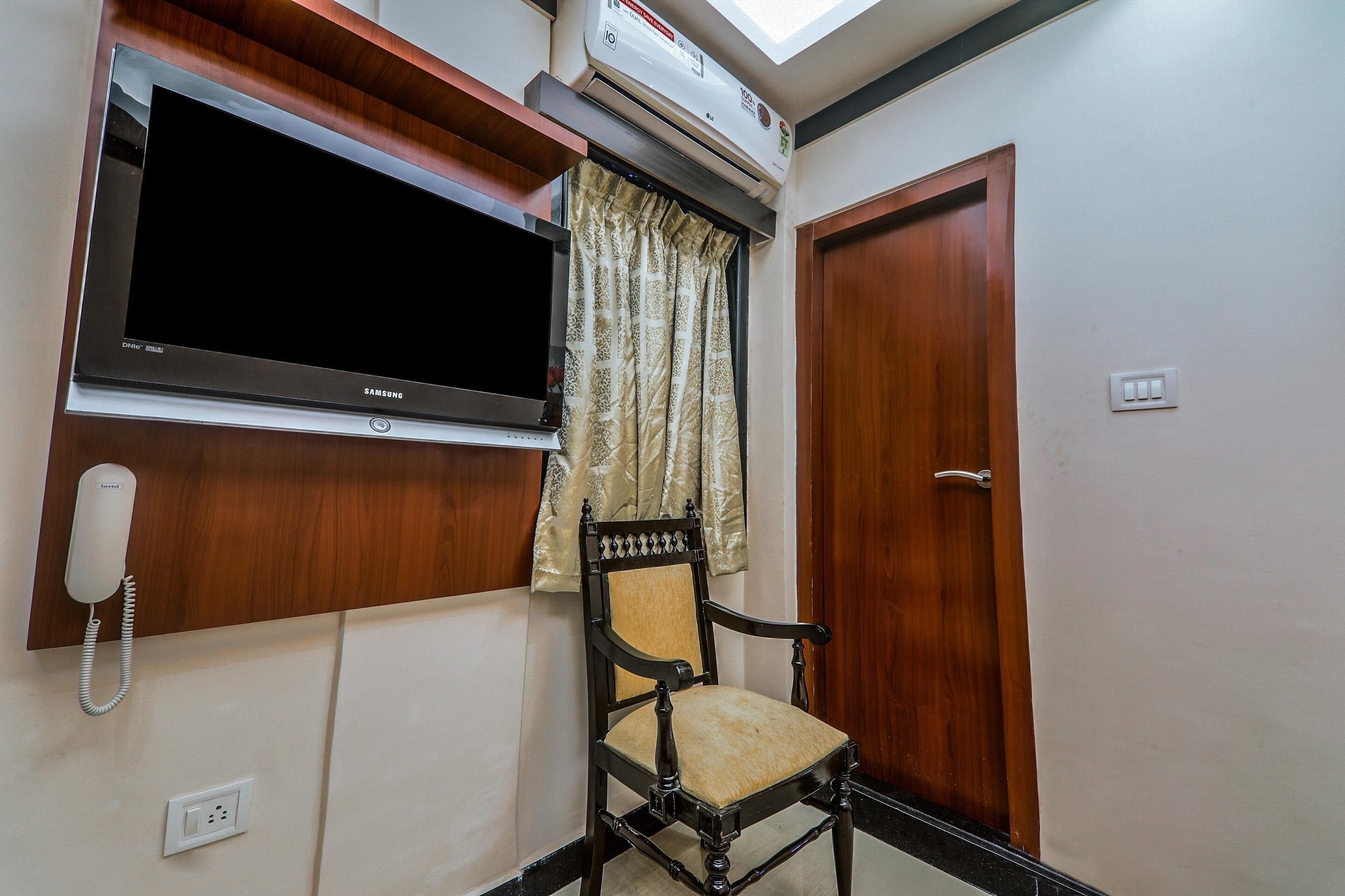 A room with a mounted television, a telephone, a wooden door, and a window with curtains.