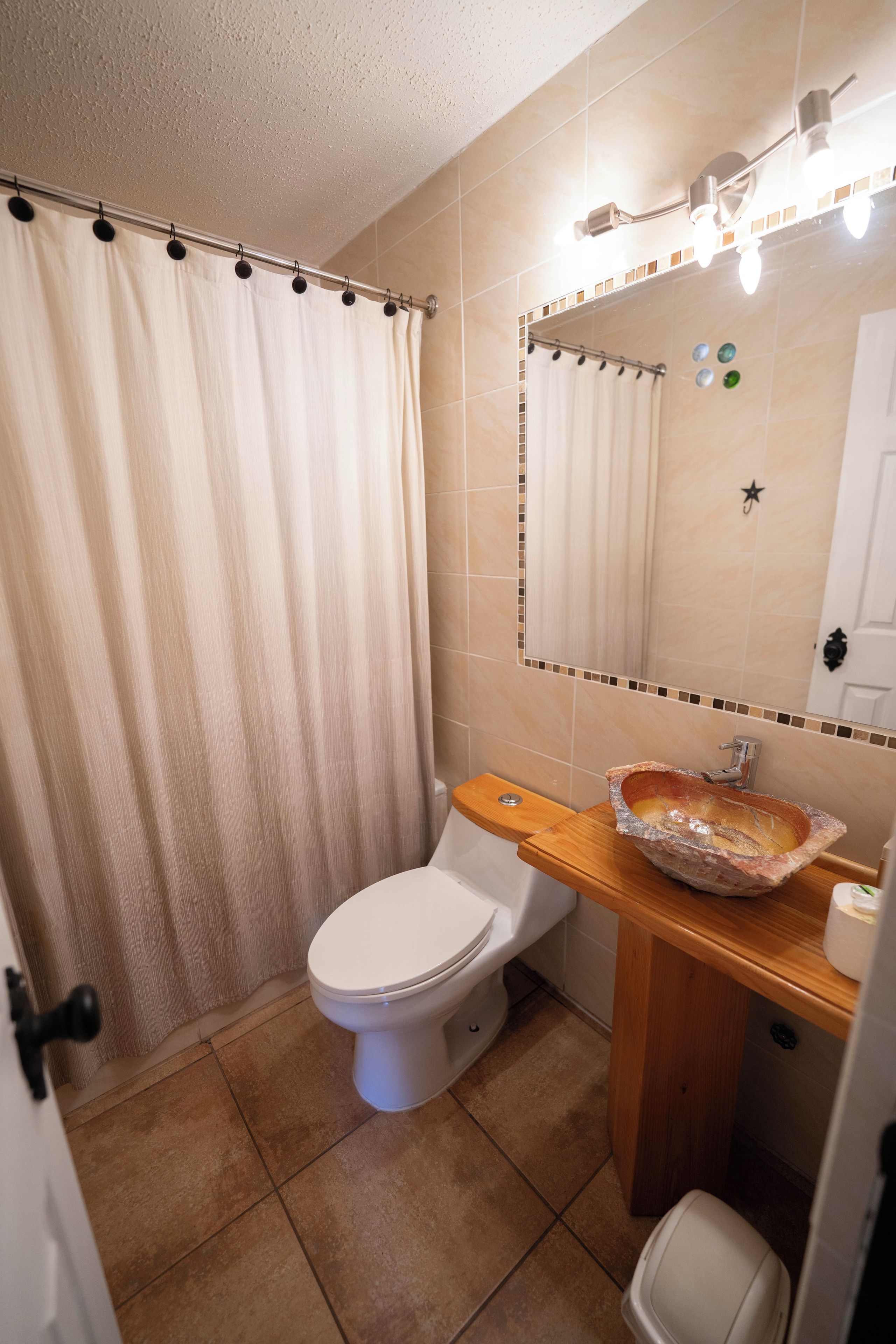 Un baño con inodoro, lavabo de piedra, espejo con iluminación y cortina de ducha.