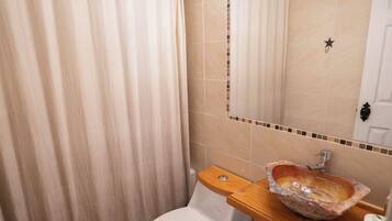 Un baño con inodoro, lavabo de piedra, espejo con iluminación y cortina de ducha.