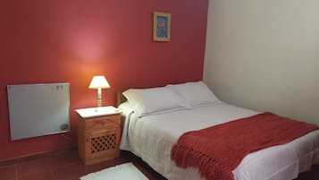 A bedroom with a bed, a nightstand, a lamp, a picture on the wall, and a red blanket.