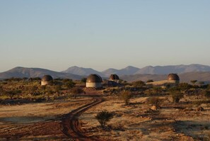 A desert landscape with three dome-shaped structures, a dirt path leading to them, and mountains in the background.