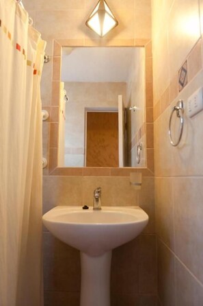 Un baño con lavamanos pedestal, espejo y cortina de ducha.