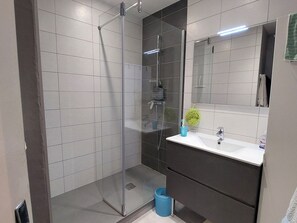 Ein modernes Badezimmer mit einer gläsernen Dusche, einem weißen Waschbecken und einem Spiegel.