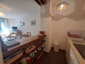 Un coin repas avec une table en bois, des chaises et un espace cuisine comprenant un évier et des placards.