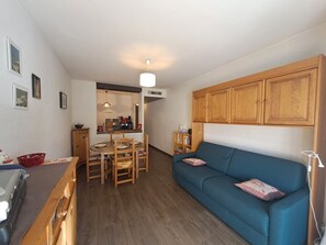 A compact living space with a dining area, a sofa, wooden cabinets, and a kitchenette. - Ideal studio near slopes - 4 guests (Les Deux Alpes)