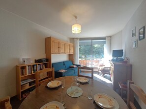 Ein Essbereich mit einem Tisch für vier Personen, einem blauen Sofa, einem Bücherregal und einem Fernsehgerät auf einem Schrank.