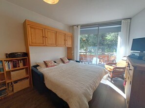 Ein Schlafzimmer mit einem Bett, einem Bücherregal, einem Fernseher und Blick ins Freie.