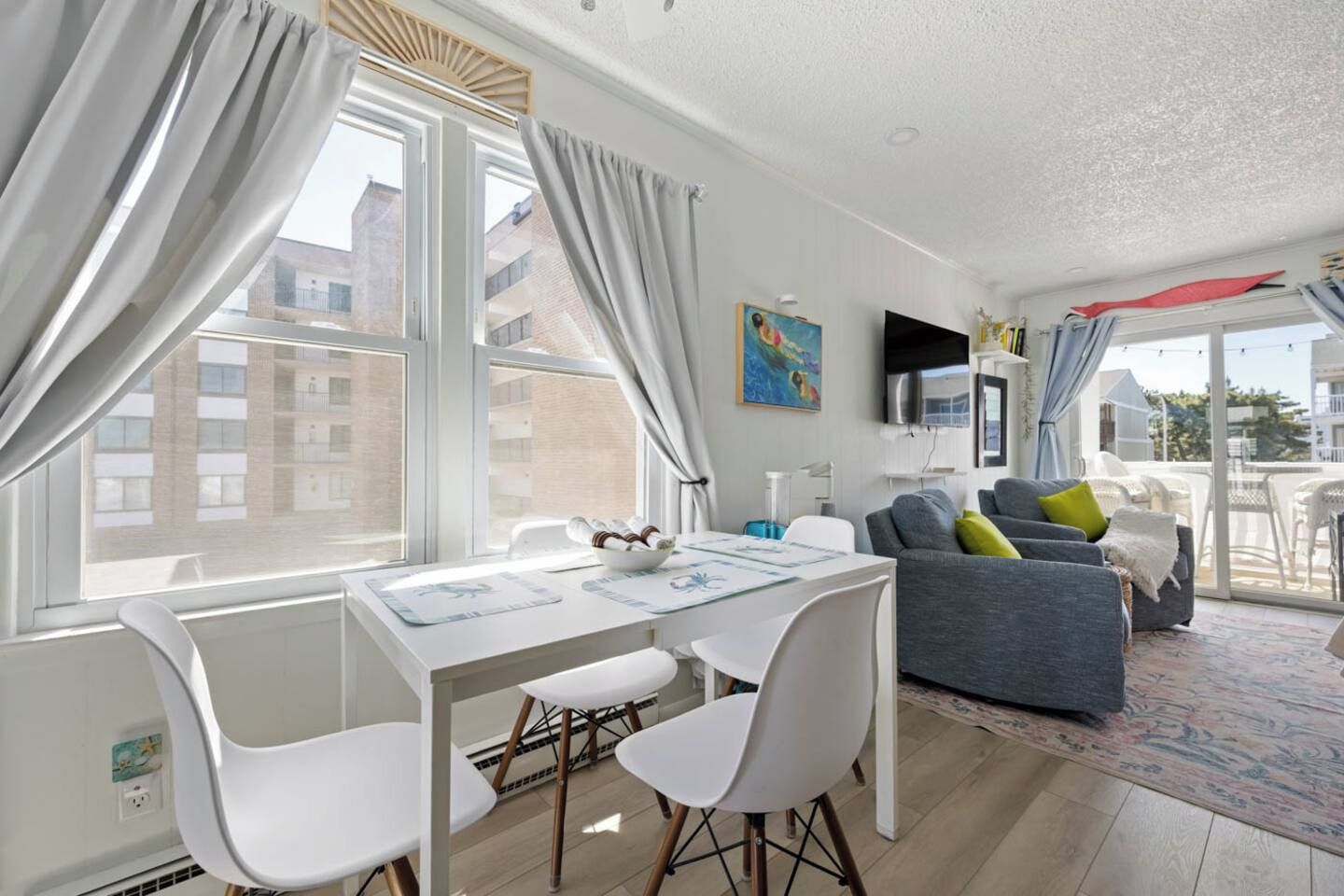 A modern living room with a dining area, large windows, and a view of buildings.