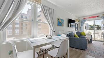 A modern living room with a dining area, large windows, and a view of buildings.