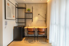 A compact kitchenette with a refrigerator, a shelf unit, and a desk with two chairs. - Nik by Bhomy (São Paulo)