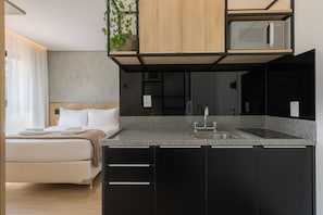 A modern hotel room with a kitchenette, a bed with white linens, and a view of the outdoors. - Nik by Bhomy (São Paulo)