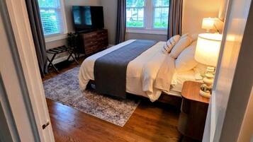 A bedroom with a bed, bedside table, lamp, TV, dresser, and windows.