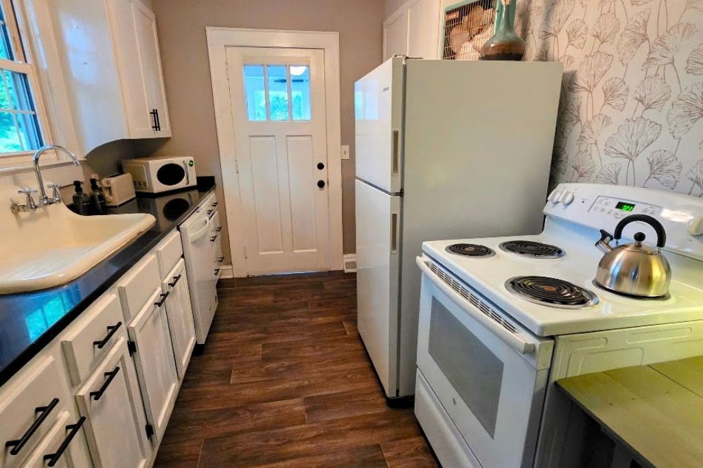 Une cuisine compacte avec des meubles blancs, un four encastré, une cuisinière et une bouilloire.