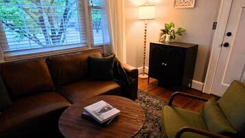 Un salon avec un canapé en cuir marron, une table basse ronde sur laquelle se trouve un magazine, un fauteuil vert, un meuble en bois foncé et un lampadaire.