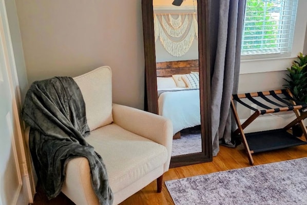 A room with a sofa, a bed with macrame headboard, a window with curtains, and a small wooden bench.