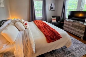 A bedroom with a bed, a television, a desk, and a window.