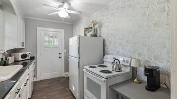 A compact kitchen with a refrigerator, stove, microwave, and a ceiling fan.